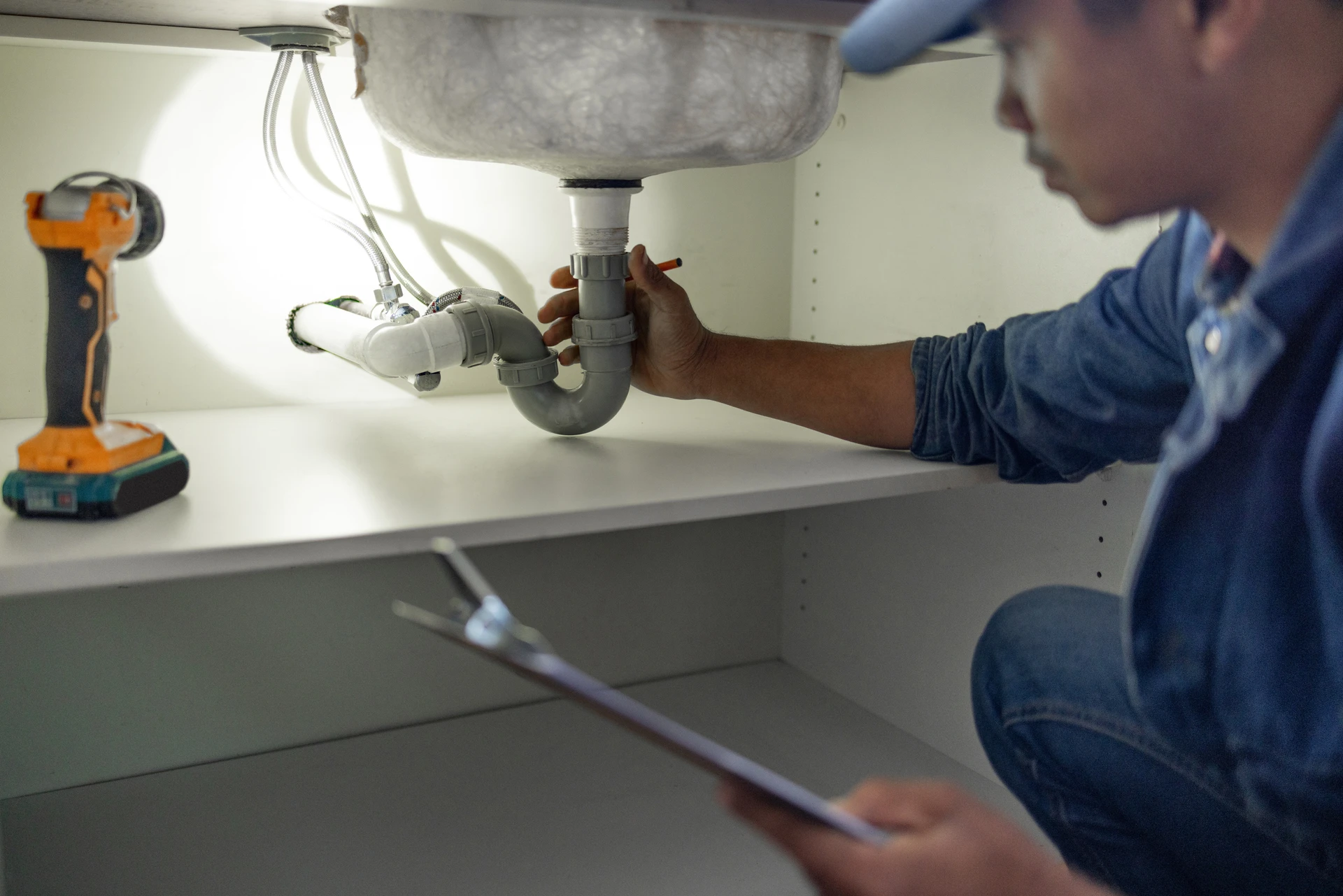 Plumber inspecting under-sink drain pipes with a checklist